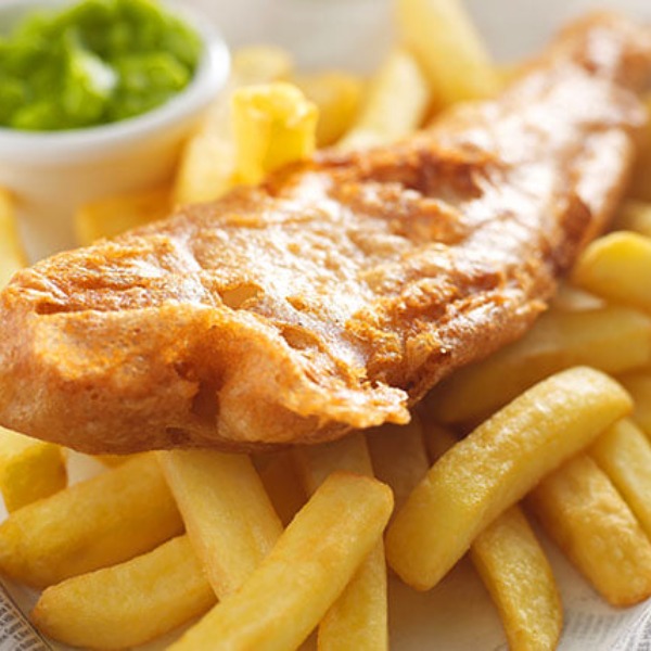 Battered cod sitting on top of chips with mushy peas in the background